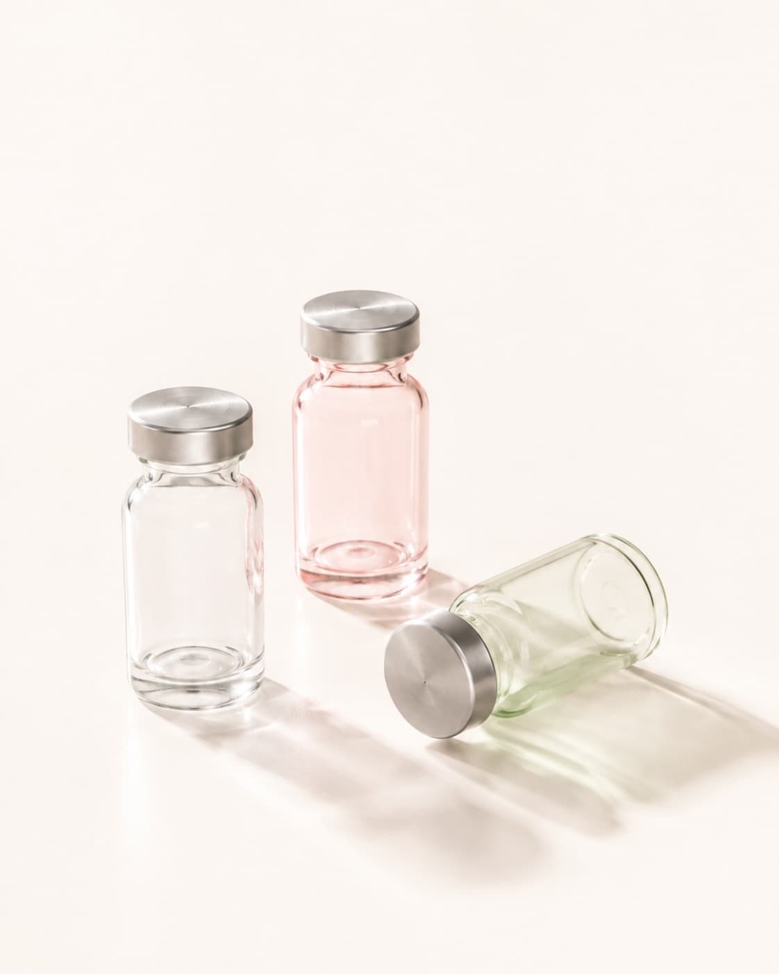 Three unlabeled glass vials with silver caps arranged on a cream surface.