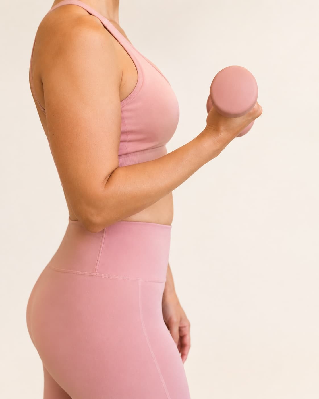 A woman in pink activewear standing in profile against a soft background.